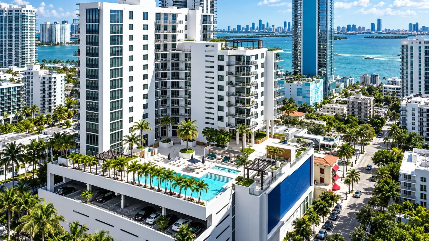 White tower with a rooftop pool deck among palms and towers